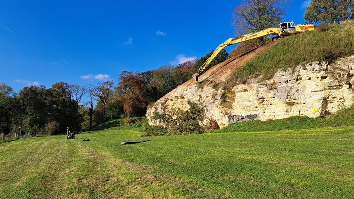 Een graafmachine schraapt een laag grond weg op een heuvel