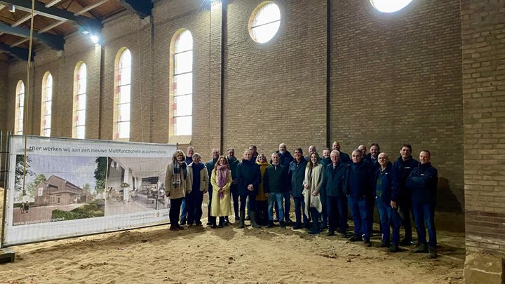 Groepsfoto van alle betrokkenen in de kerk, op een bouwbord is het nieuwe ontwerp zichtbaar